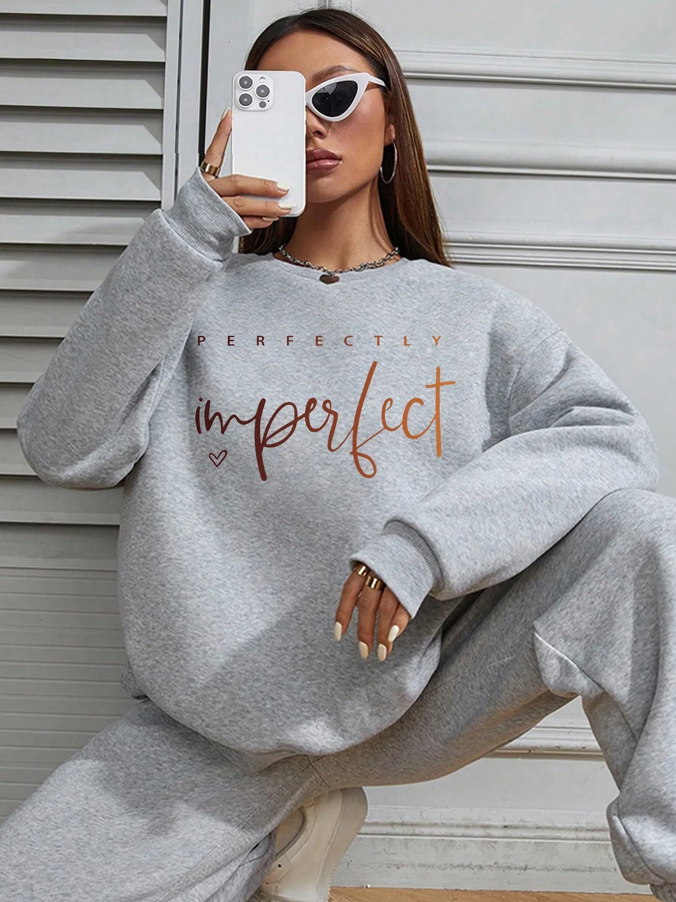 A person wearing a grey oversized sweatshirt and matching sweatpants, with the phrase "perfectly imperfect" printed on the sweatshirt in an orange and pink gradient font